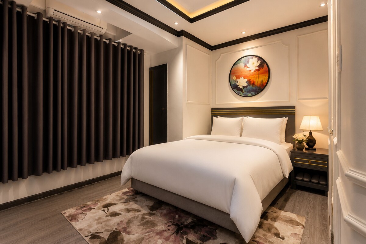 Quarto de hotel com uma cama grande, um quadro redondo na parede, uma mesa de cabeceira com abajur e uma janela com cortinas.