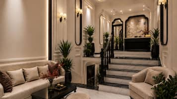 A spacious lobby with a grand staircase, a sofa, a coffee table, and decorative plants.