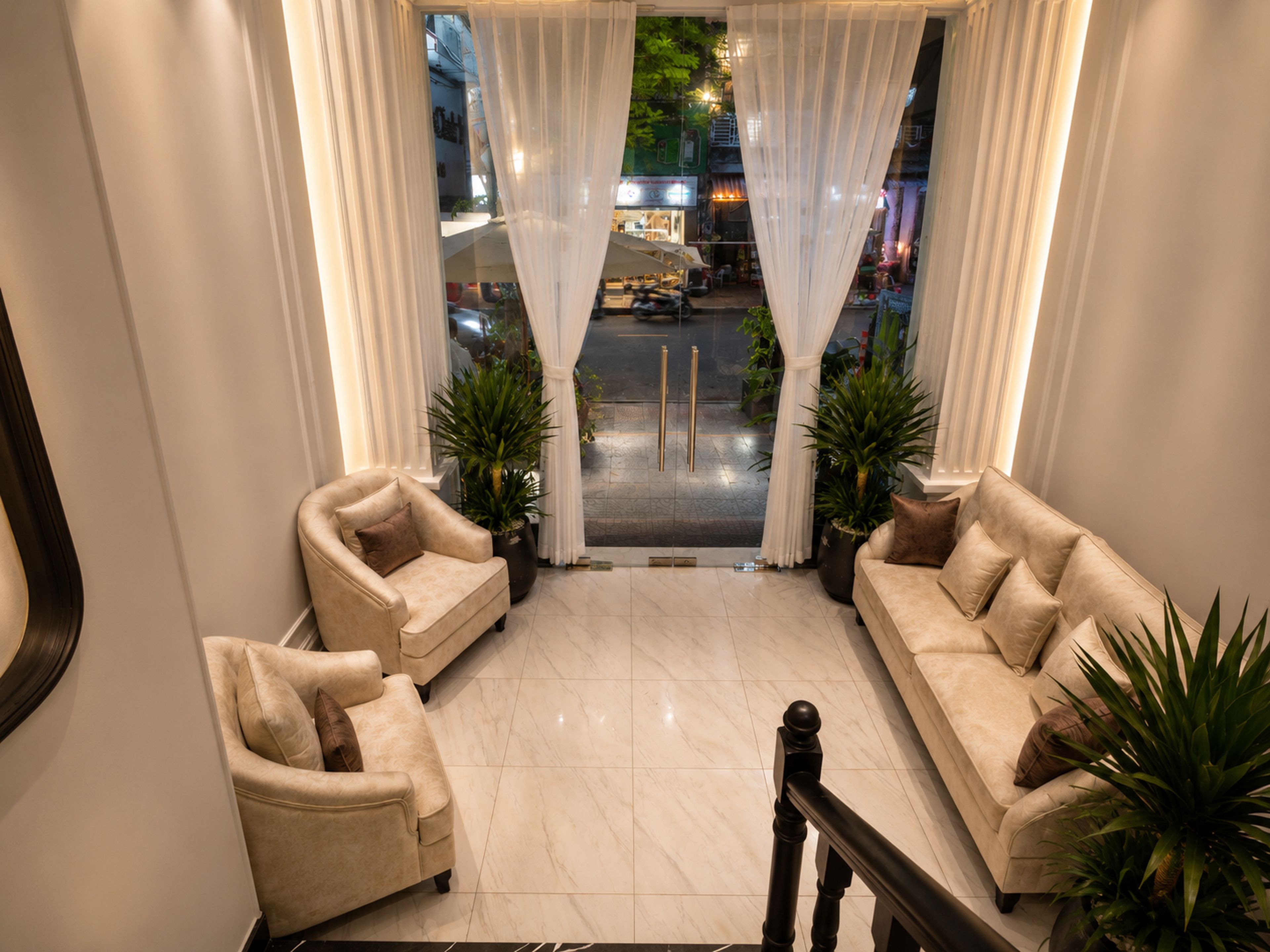 Um saguão de hotel com dois sofás, uma escadaria e vista para a rua.