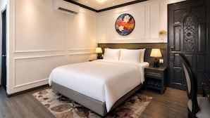 Quarto de hotel com uma cama grande, mesa de cabeceira com abajur, painel decorativo na parede e porta com design elaborado.