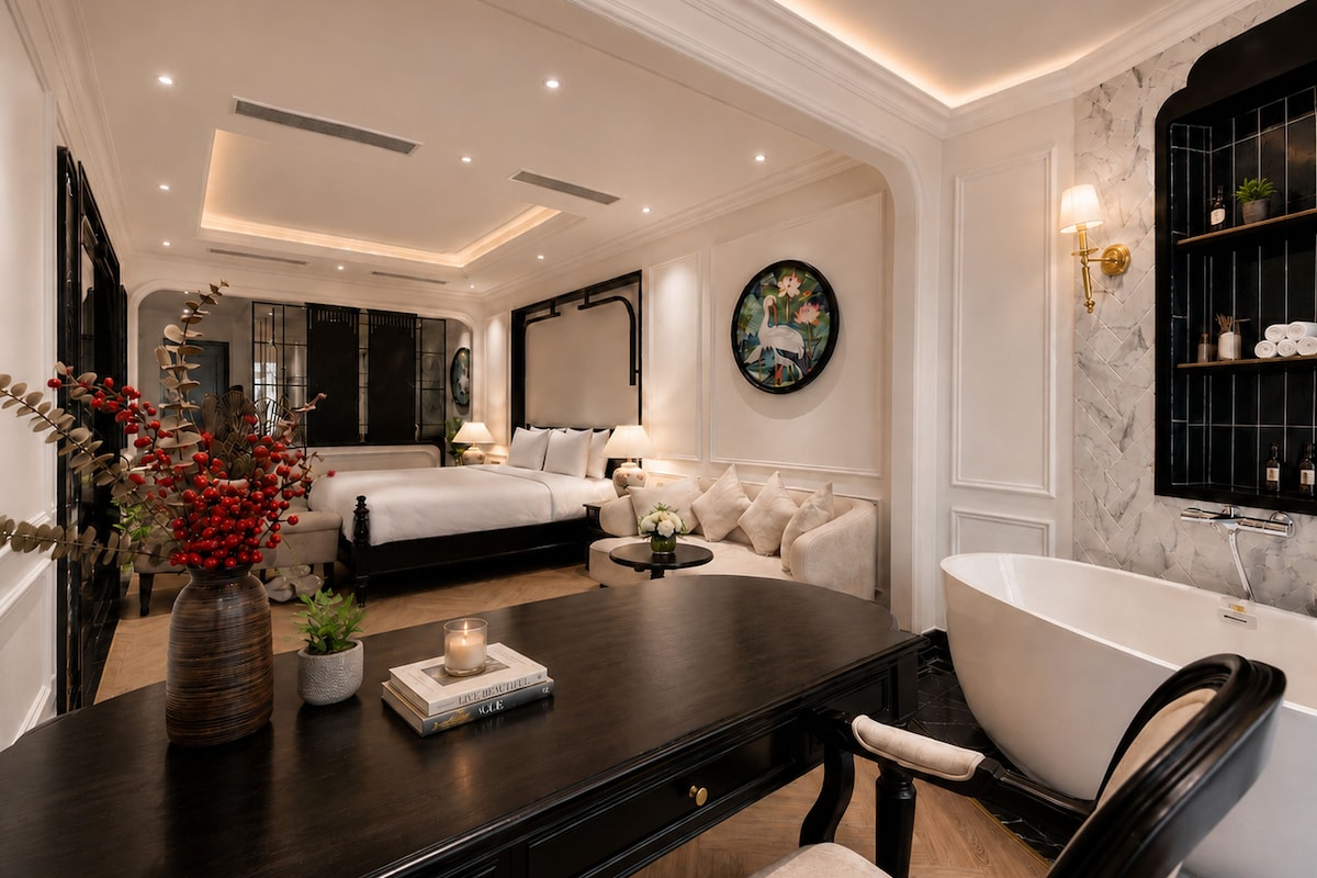 Quarto de hotel moderno com cama grande, área de estar com mesinha de centro, banheira e prateleira fixada na parede com artigos de higiene pessoal.