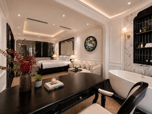 Quarto de hotel moderno com cama grande, área de estar com mesinha de centro, banheira e prateleira fixada na parede com artigos de higiene pessoal.