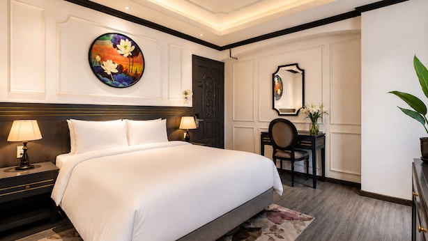Quarto de hotel com uma cama grande, uma escrivaninha, uma cadeira, um quadro redondo e um espelho na parede.