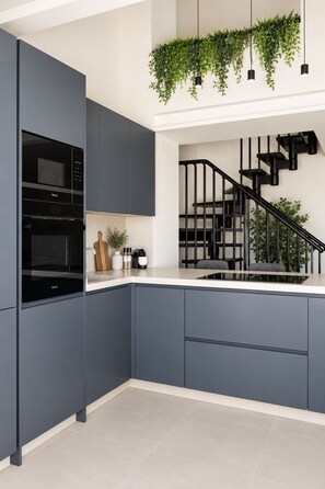 A modern kitchen with dark cabinetry, a built-in oven, and a staircase with black railings. - Luxury Penthouse | Private Terrace & Sea Views (Marbella)
