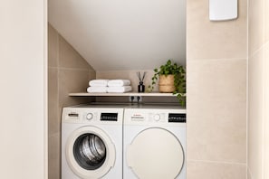 A compact laundry area with two Bosch washing machines, a shelf with folded towels, a potted plant, and a wall-mounted soap dispenser. - Luxury Penthouse | Private Terrace & Sea Views (Marbella)