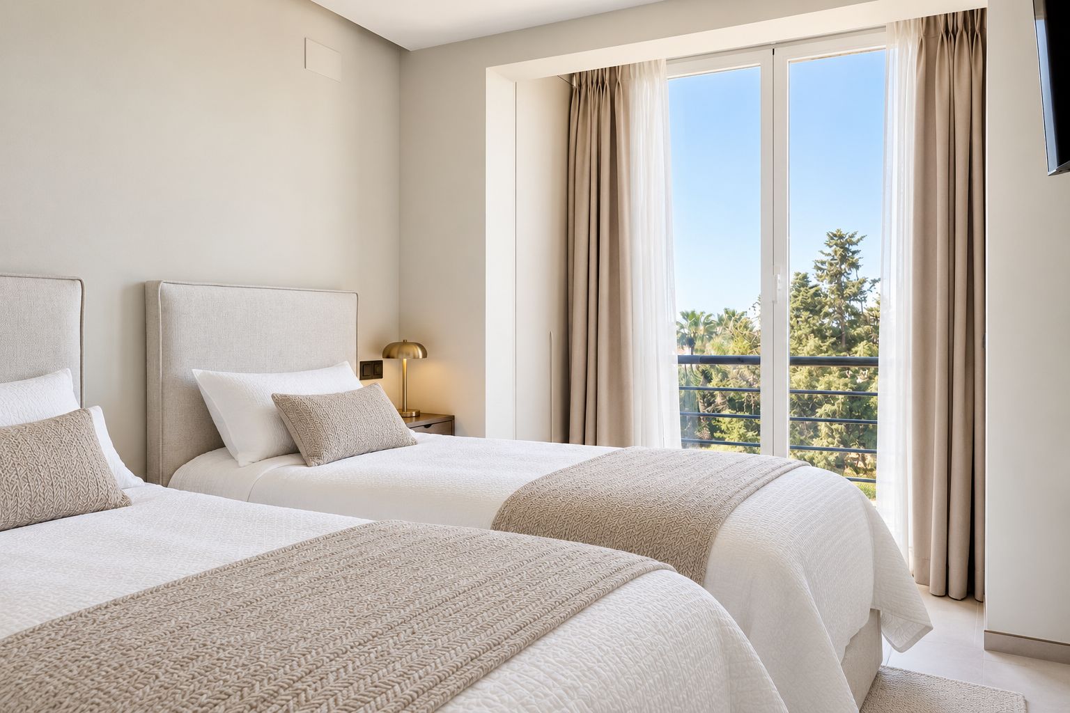 A hotel room with two beds, a nightstand, a lamp, and a balcony with curtains.
