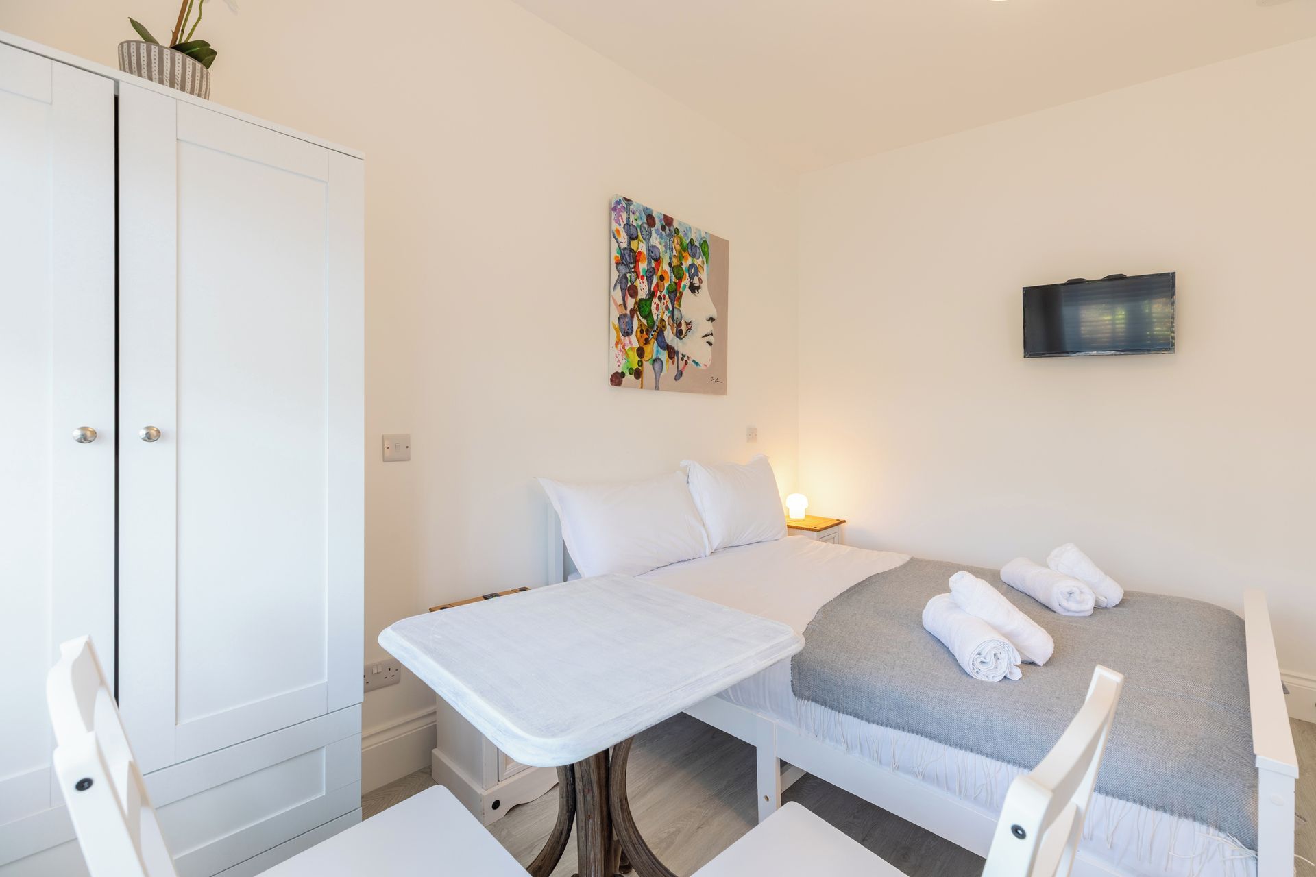 Une petite pièce propre, avec un lit, une table et une armoire.