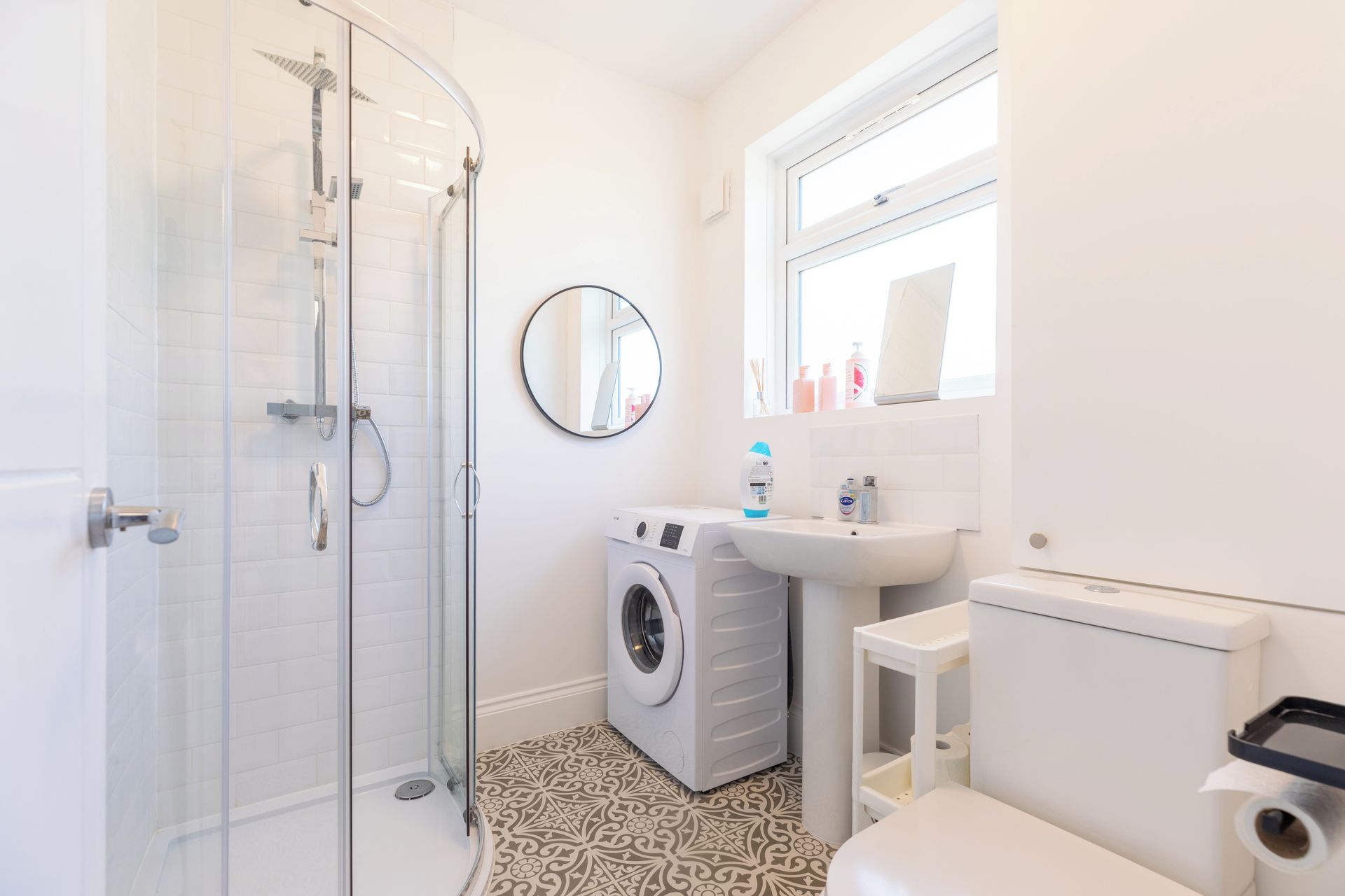 A bathroom with a glass-enclosed shower, a washing machine, a sink, and a toilet.
