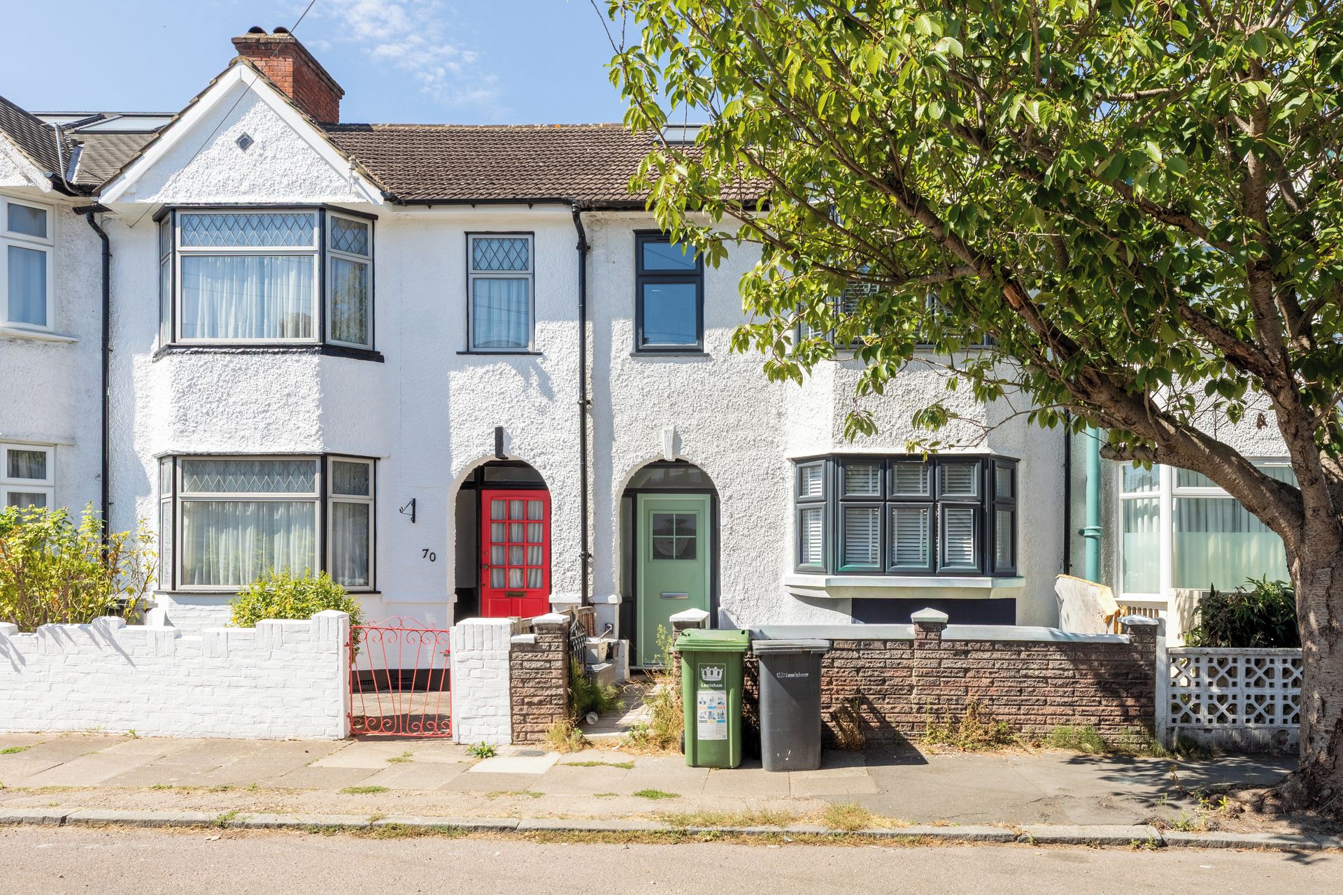 A two-story house with a red door, a bay window, and a brick wall.