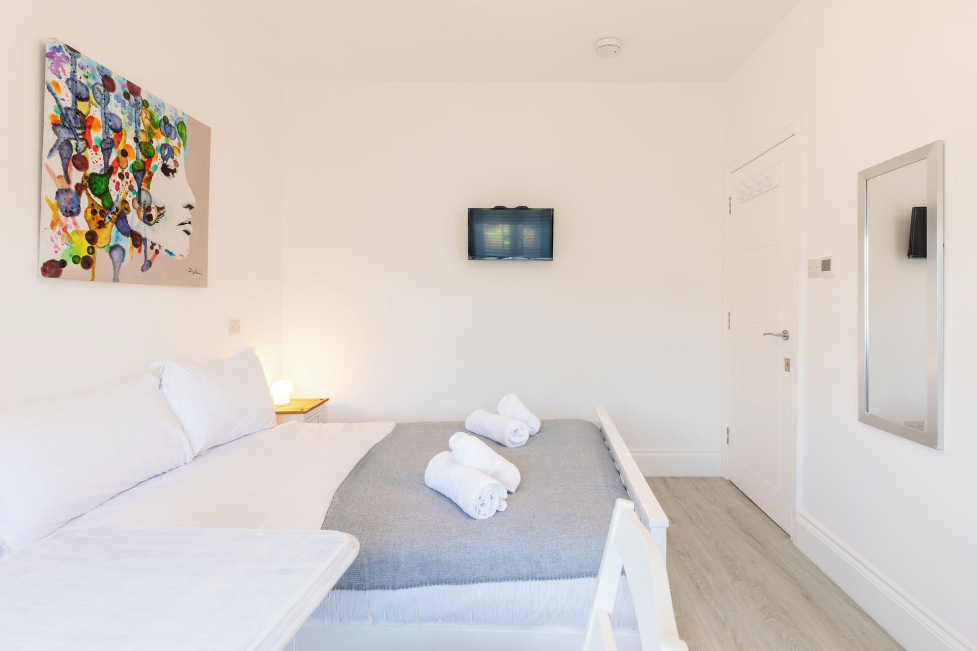 Una habitación de hotel con una cama, un televisor montado en la pared y una puerta.