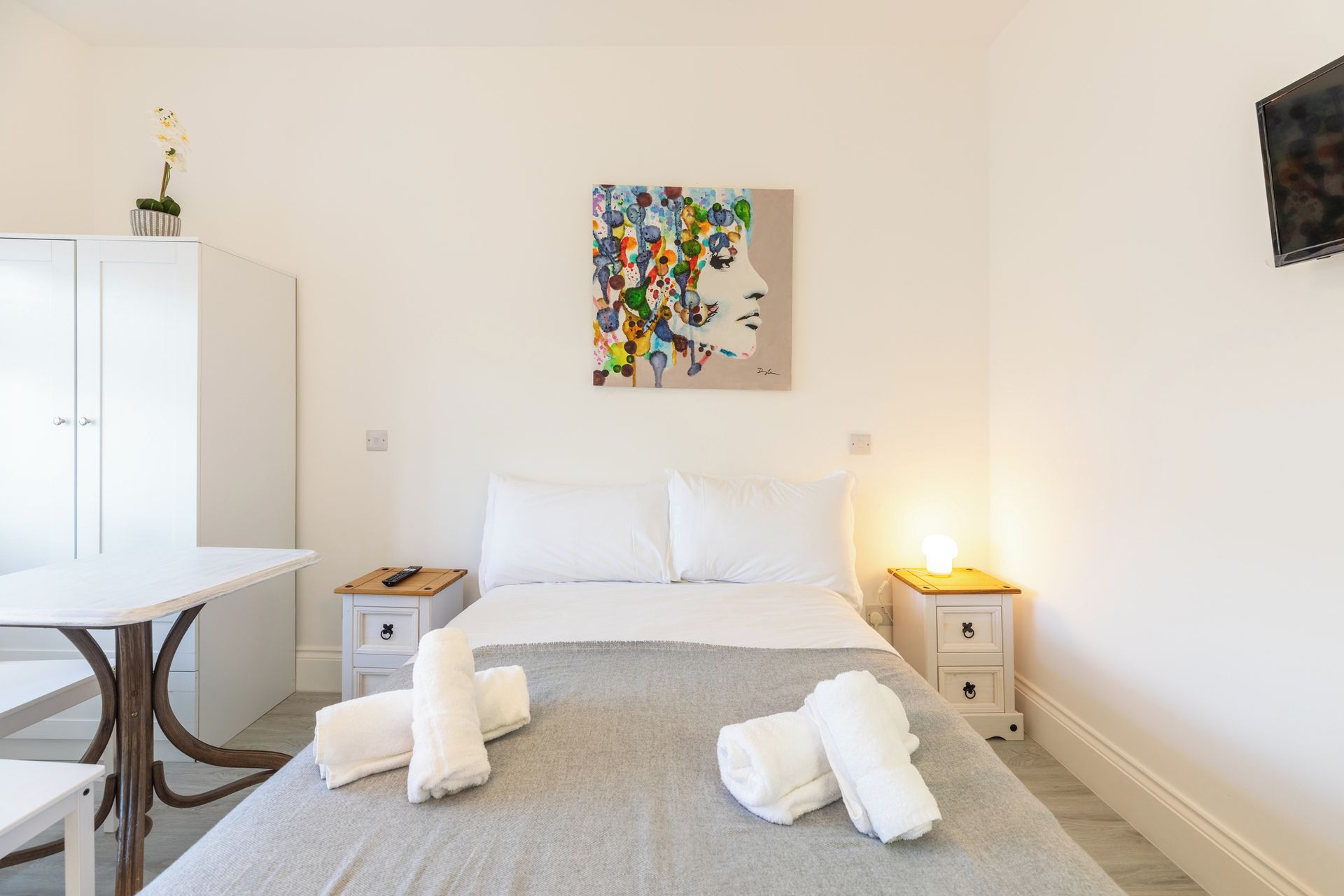 Ein Hotelzimmer mit einem Bett, Nachttischen, einem Schreibtisch und einem Bild an der Wand.