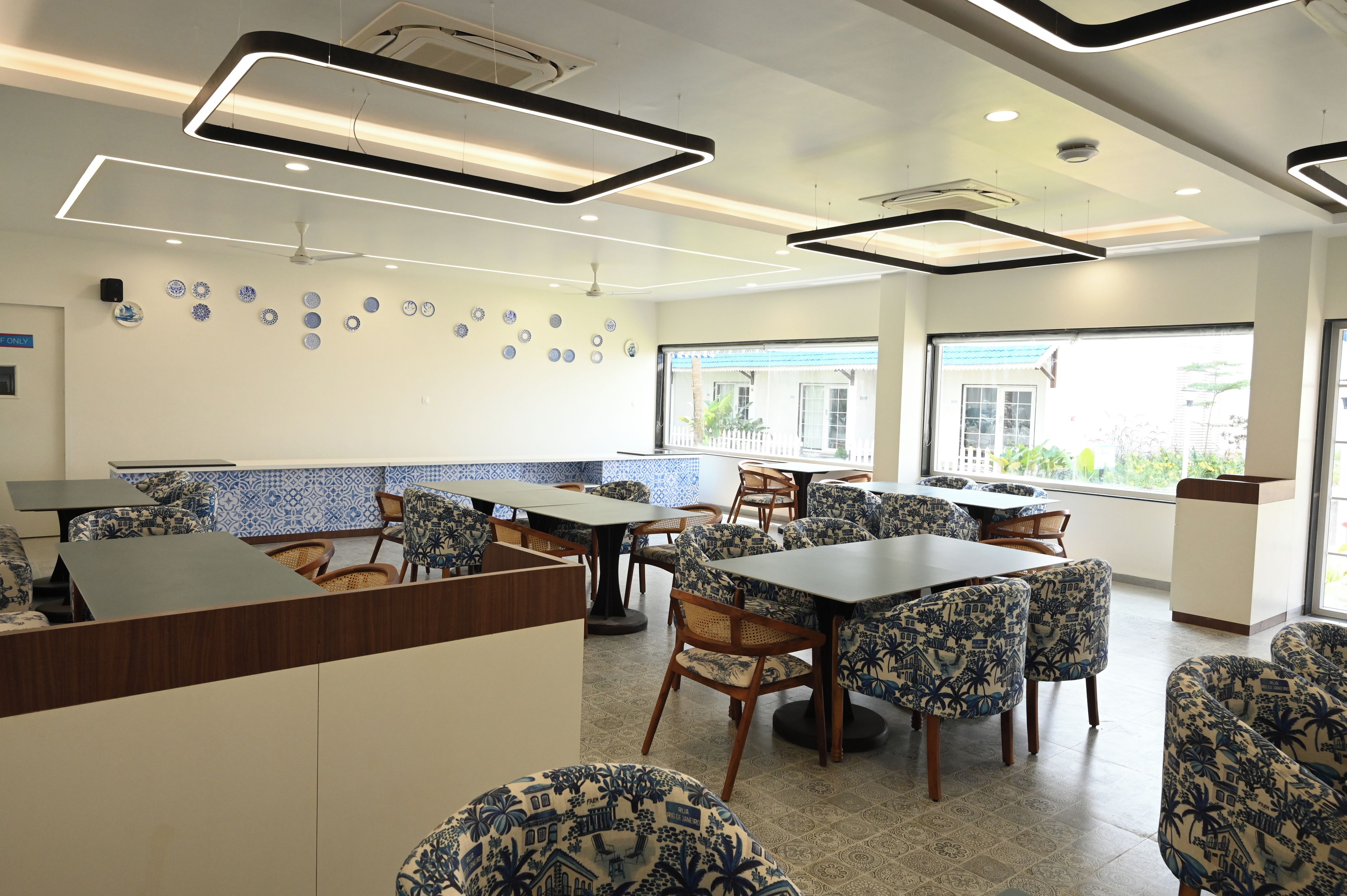 A restaurant with a modern interior, featuring a mix of patterned and plain tablecloths, wooden chairs, and a tiled floor.
