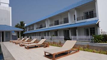 A hotel with multiple floors, a pool area with lounge chairs, and a white picket fence.