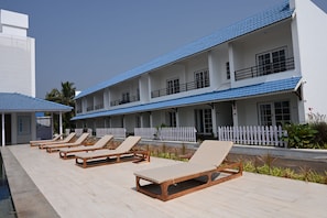 A hotel with multiple floors, a pool area with lounge chairs, and a white picket fence.