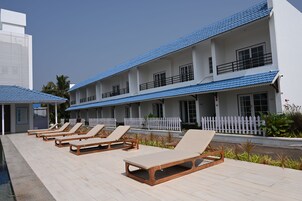 Un hotel con varios pisos, un área de piscina con sillas de descanso y una cerca blanca de piquete.
