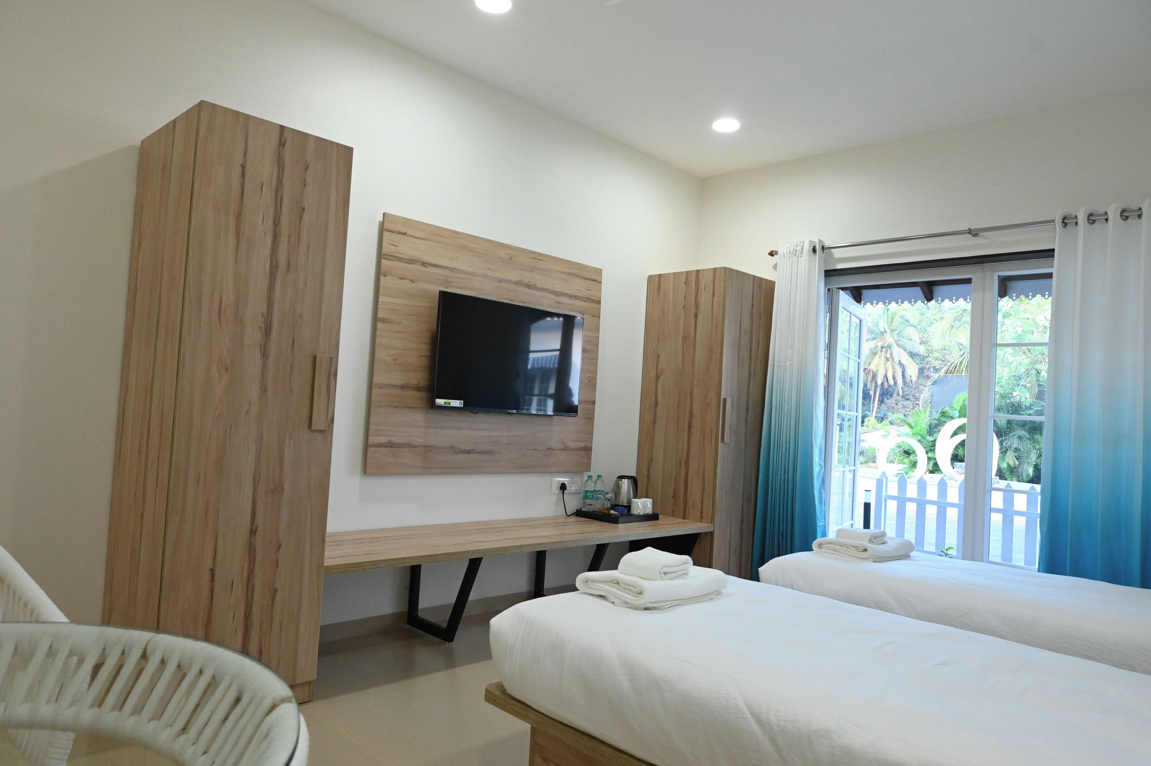 Una habitación de hotel con cama, escritorio, televisor y ventana con cortinas.