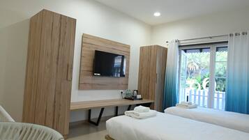 Una habitación de hotel con cama, escritorio, televisor y ventana con cortinas.