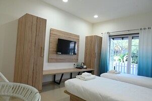 Una habitación de hotel con cama, escritorio, televisor y ventana con cortinas.