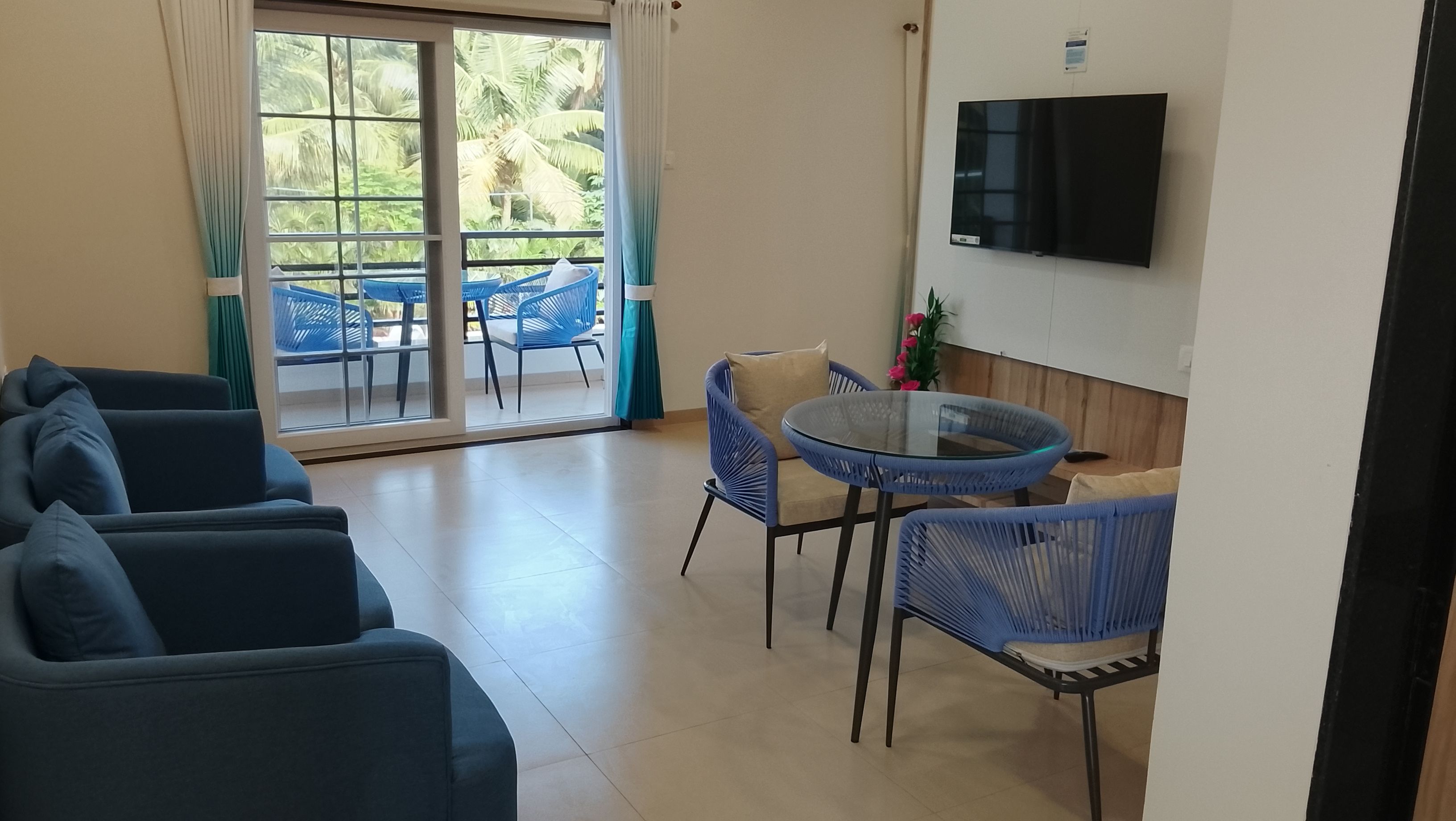 A living area with a sofa set, a round glass table, and blue chairs.