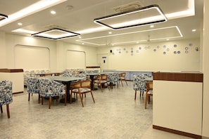 A restaurant with multiple tables and chairs, a ceiling with recessed lighting, and a wall decorated with plates.