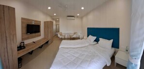 A hotel room with a bed, a TV mounted on the wall, a small table with chairs, and a window with curtains.