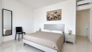 Un dormitorio moderno con cama, mesitas de noche, una silla, un espejo grande y un aire acondicionado instalado en la pared.