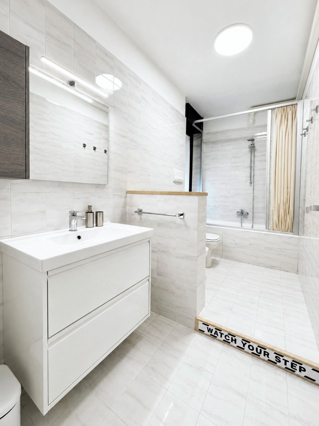 Un bagno moderno con un mobile lavabo bianco, cabina doccia in vetro e un portasciugamani a vista.