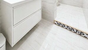 Un baño moderno con un tocador blanco, cabina de ducha con mampara de vidrio y un toallero a la vista.