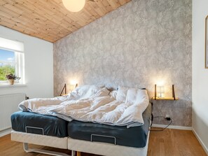 A bedroom with a bed, bedside lamps, a window with a view, and a wooden ceiling. - "Heilo" -  from the sea by Interhome (Storvorde)