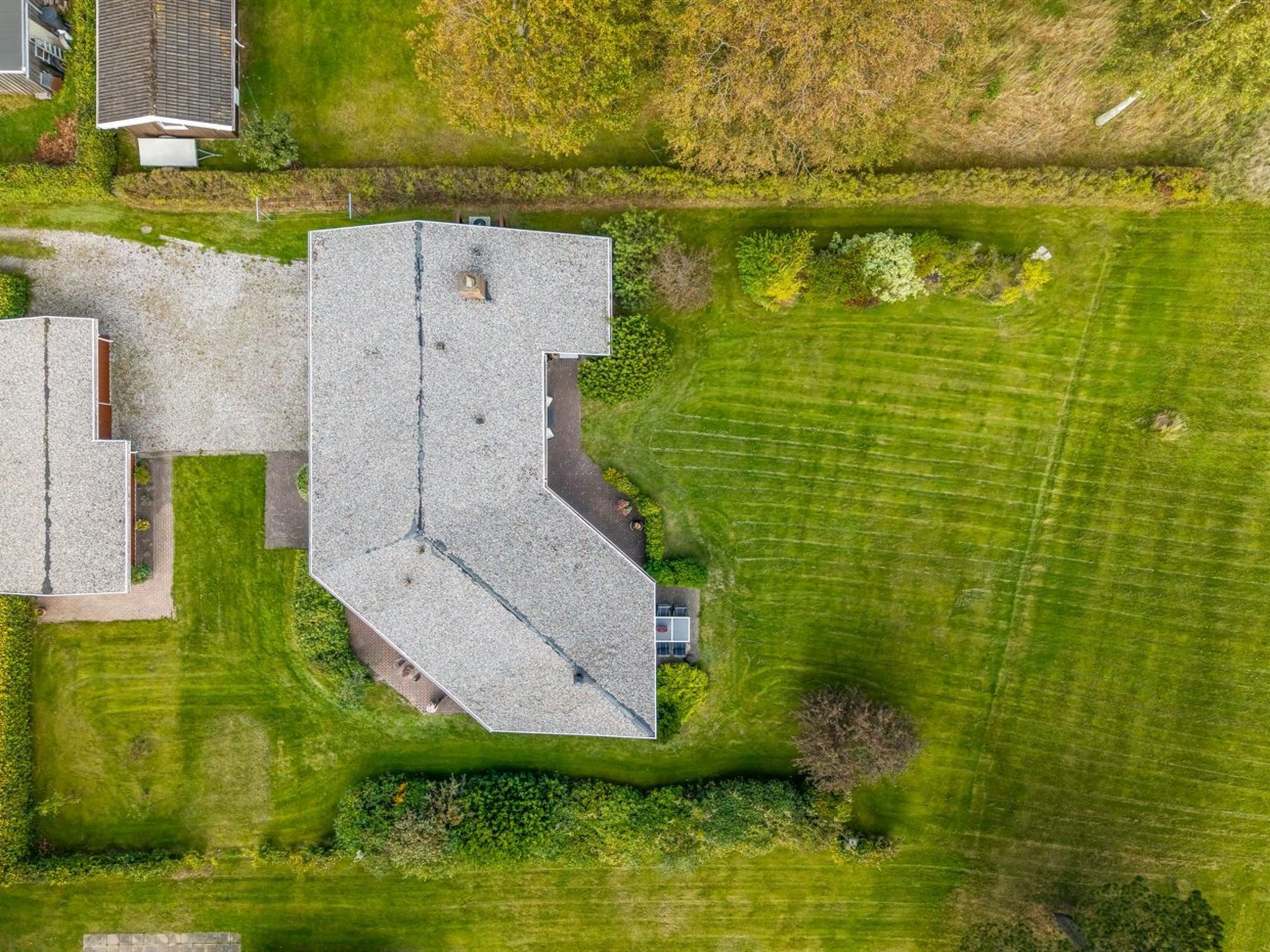 Une vue aérienne d’une propriété comprenant un grand bâtiment, une construction plus petite attenante et une pelouse bien entretenue.
