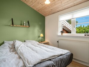 A bedroom with a bed, a nightstand with a lamp, a window with a view of greenery, and a wooden ceiling. - "Heilo" -  from the sea by Interhome (Storvorde)