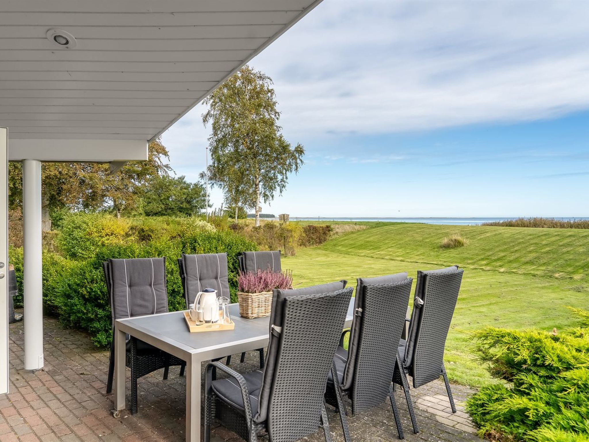Une terrasse extérieure avec une table et des chaises, une vue sur la mer et un paysage verdoyant.