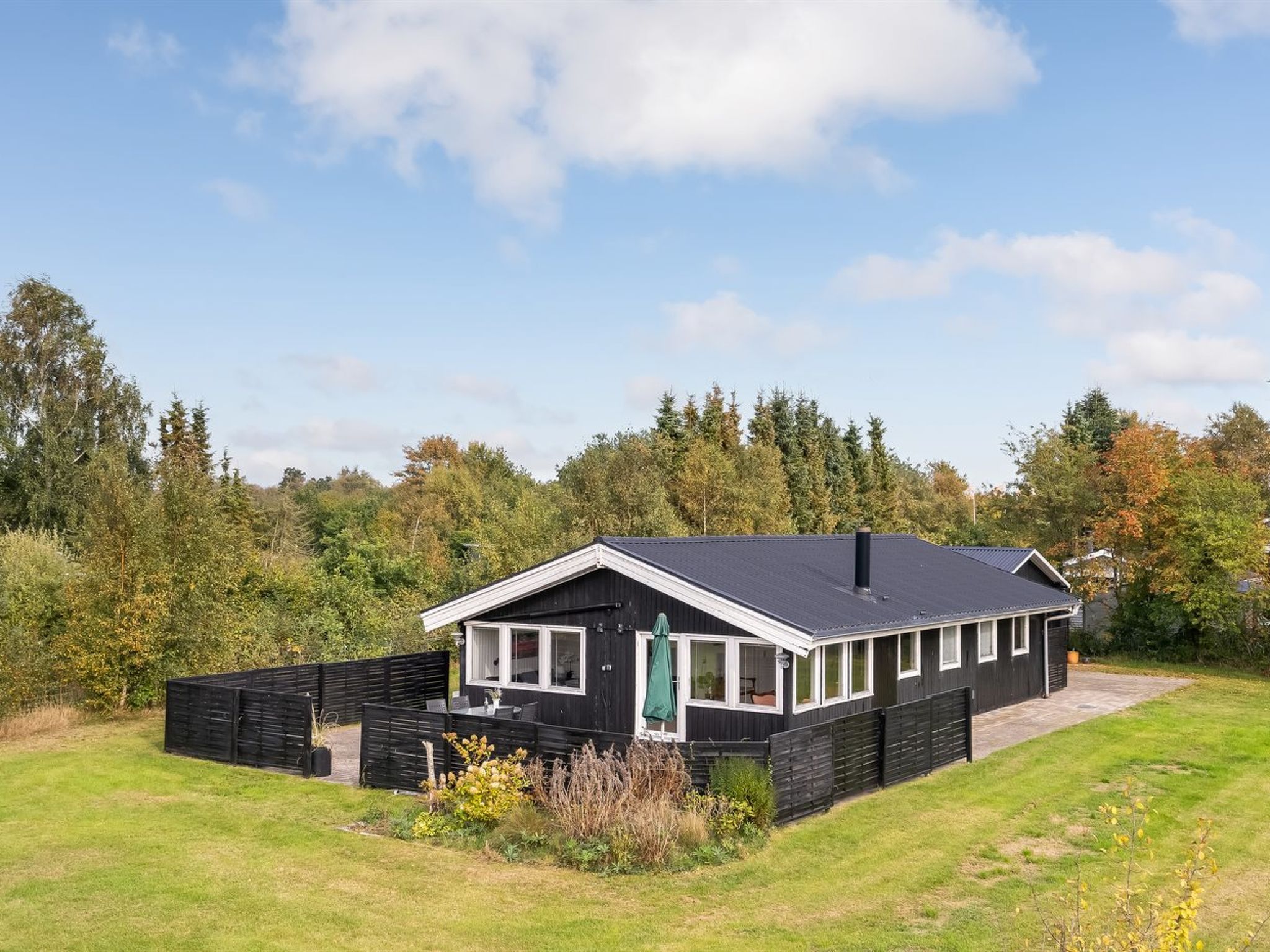 A single-story building with a dark exterior, a sloped roof, and a fenced yard.