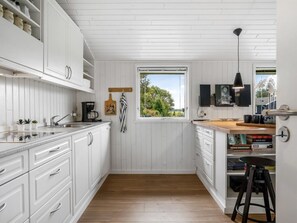 A modern kitchen with white cabinetry, a wooden countertop, and a window providing a view of greenery. - "Grith" - 740m to the fjord by Interhome (Storvorde)