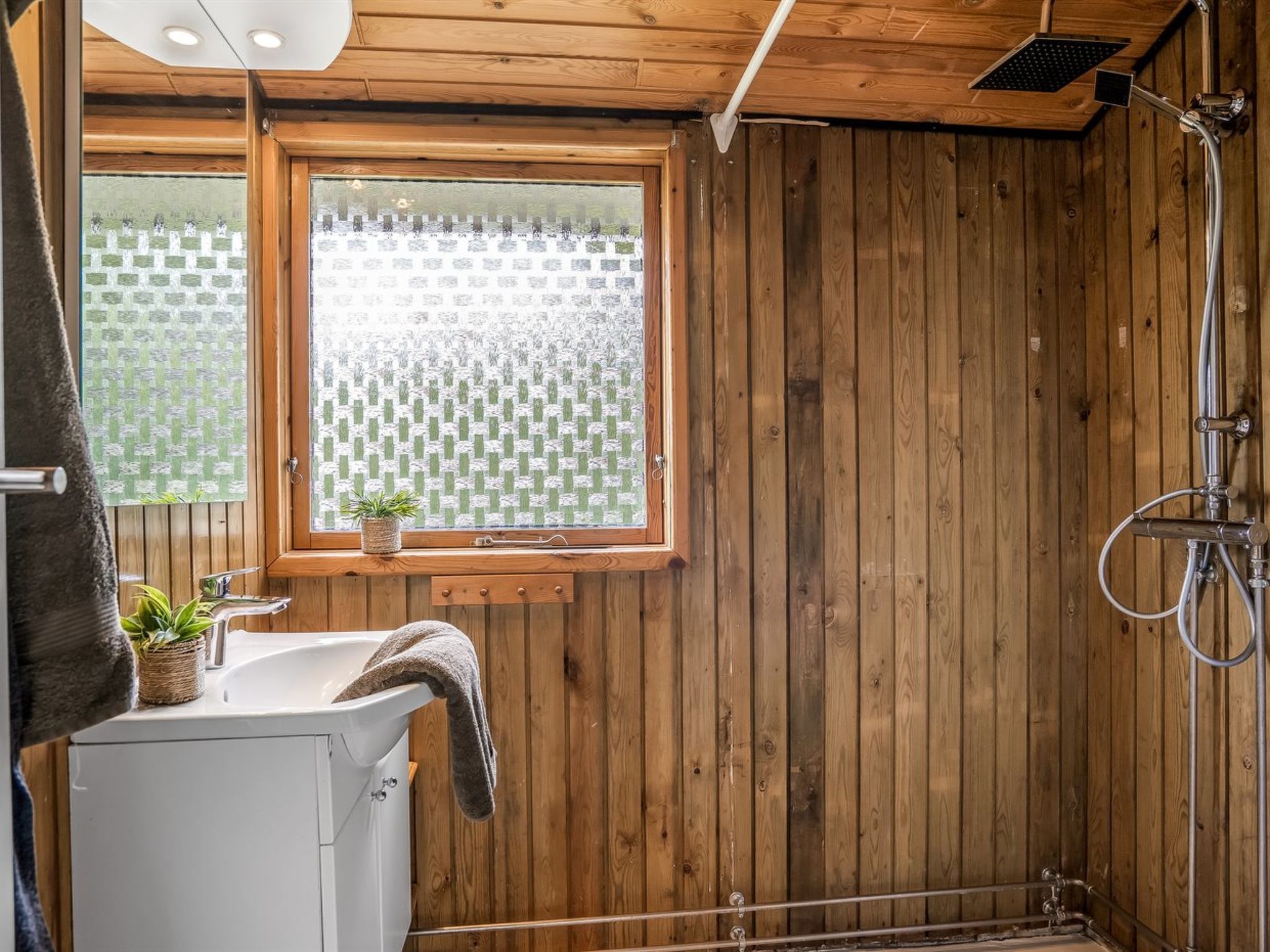 Een houten interieur met een douche, een wastafel en een raam met uitzicht.