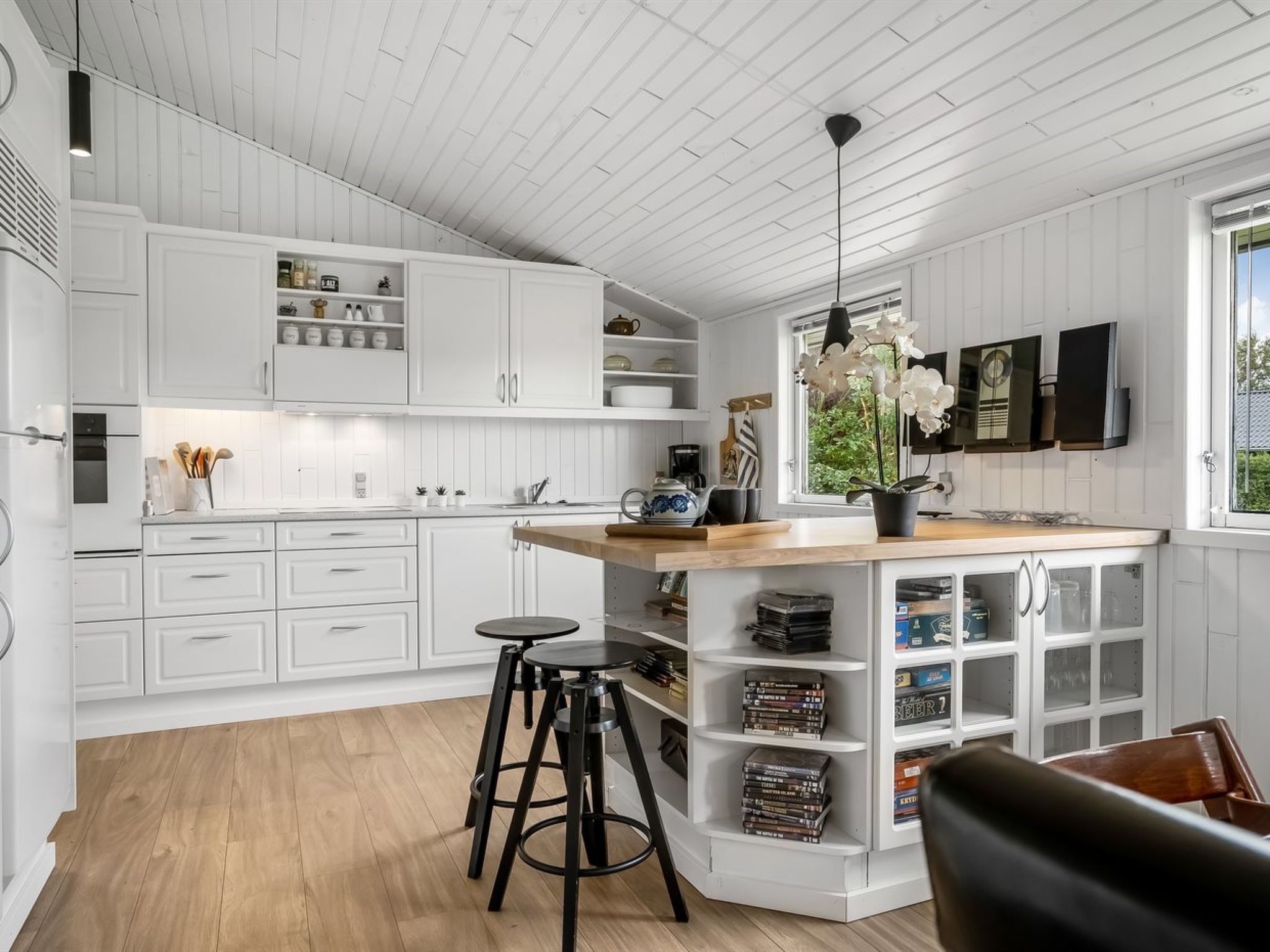 Cozinha moderna com armários brancos, uma ilha de madeira e um espaço de bar com banquetas.