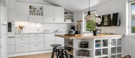 Cozinha moderna com armários brancos, uma ilha de madeira e um espaço de bar com banquetas.