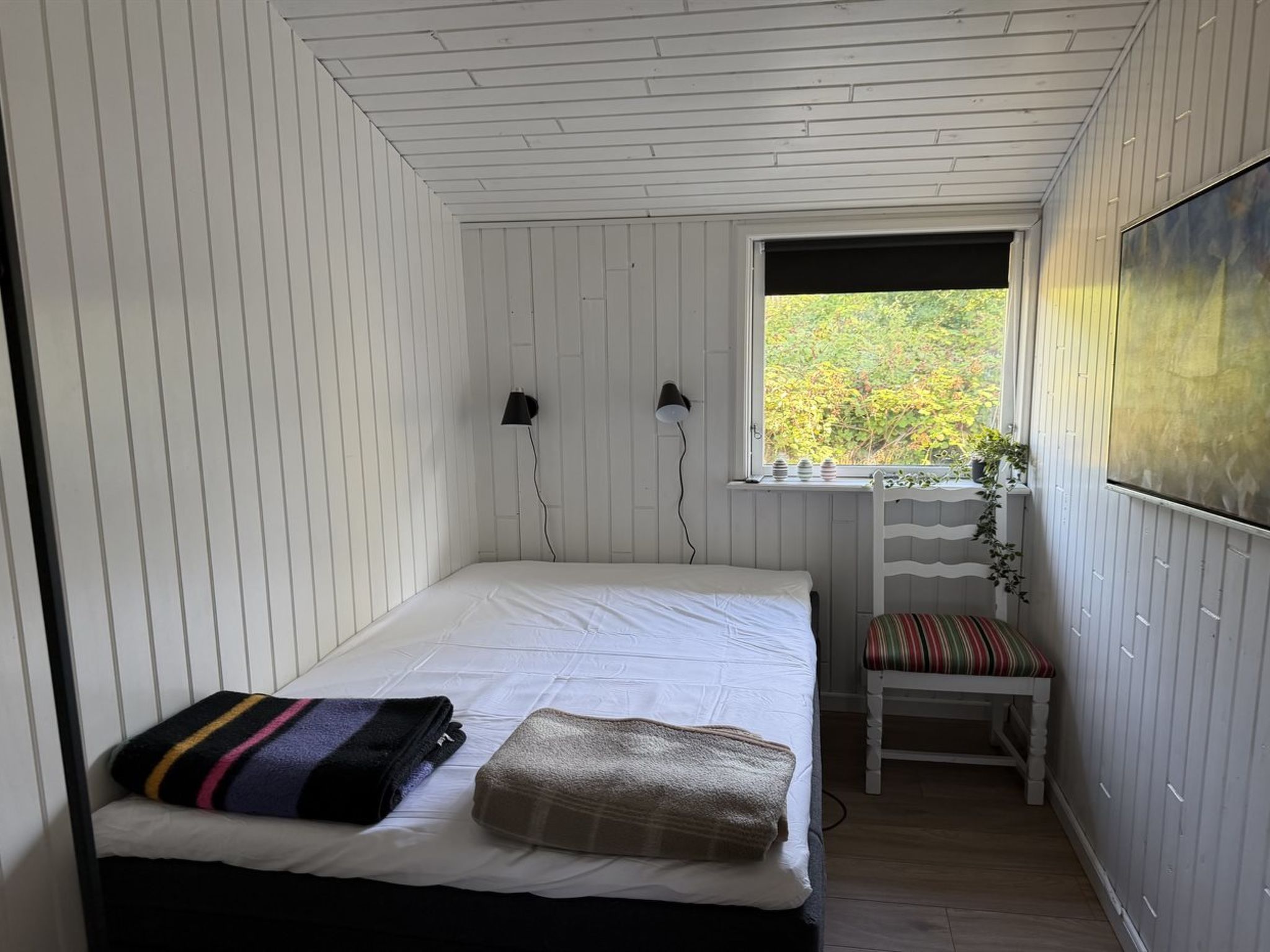 Un dormitorio con una cama, un banco, un ventanal y dos lámparas de pared.