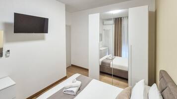 Et hotelværelse med en seng, et natbord, et fjernsyn ophængt på væggen og et spejl.