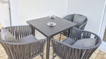 En terrasse med et firkantet bord og fire fletstole.