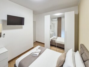 Een hotelkamer met een bed, nachtkastje, televisie aan de muur en een spiegel.