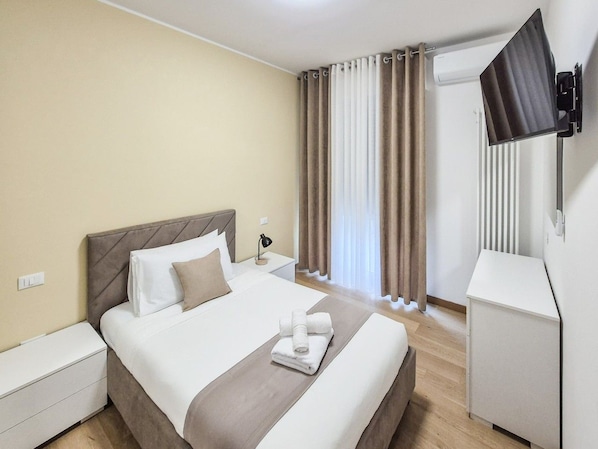 Een hotelkamer met een bed, nachtkastje, lamp en een aan de muur bevestigde televisie.