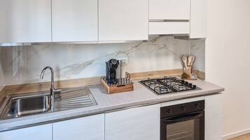 Cozinha moderna com pia de aço inoxidável, máquina de café embutida, fogão a gás e lava-louças.