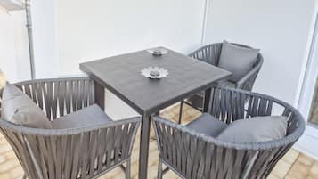 Un patio con una mesa cuadrada y cuatro sillas de mimbre.