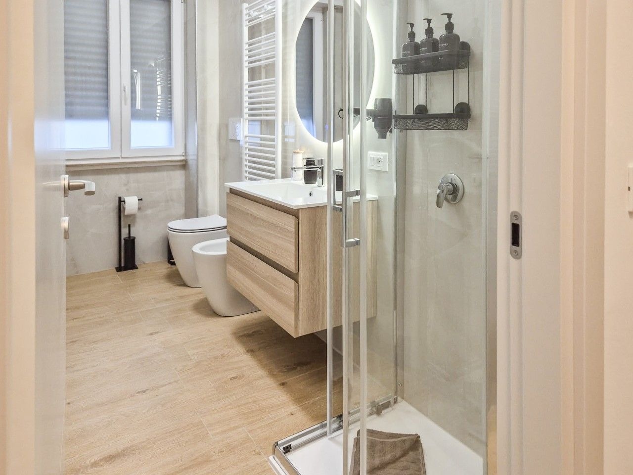 A modern bathroom with a glass shower enclosure, a wooden vanity, and a toilet.