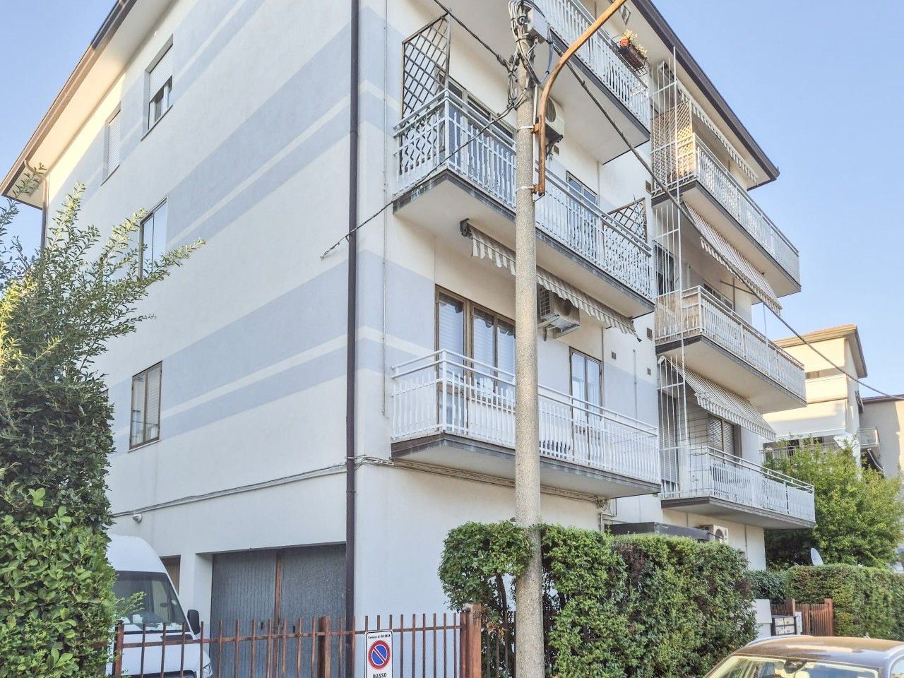 Un edificio residencial de varios pisos con balcones, una entrada porticada y un cielo despejado.