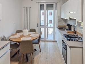 A modern kitchen with a round dining table, chairs, a stove, and a window with blinds.