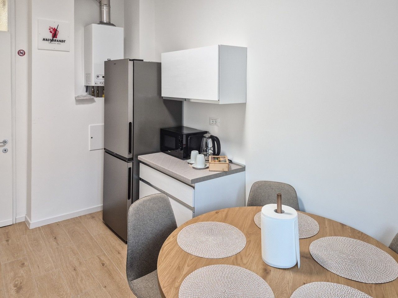 Cocina compacta con refrigerador, microondas y cafetera. Hay una mesa de comedor con individuales y una vela blanca.