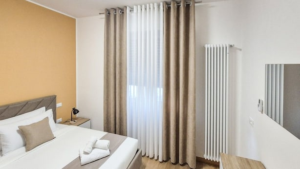 Una camera d'albergo con un letto, tende, un termosifone e un comodino.