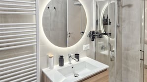 Un bagno moderno con un lavandino bianco, uno specchio rotondo e un box doccia in vetro.